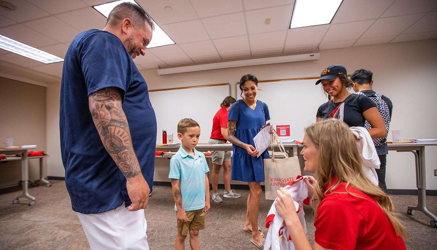 Ferguson, right, presents a gift Iowa State youth tee shirt to Landon Motter, 6, of Des Moines, while his father, Scott, mother, Kaitlyn, and incoming student and big sister, Mariah Motter look on during orientation registration.